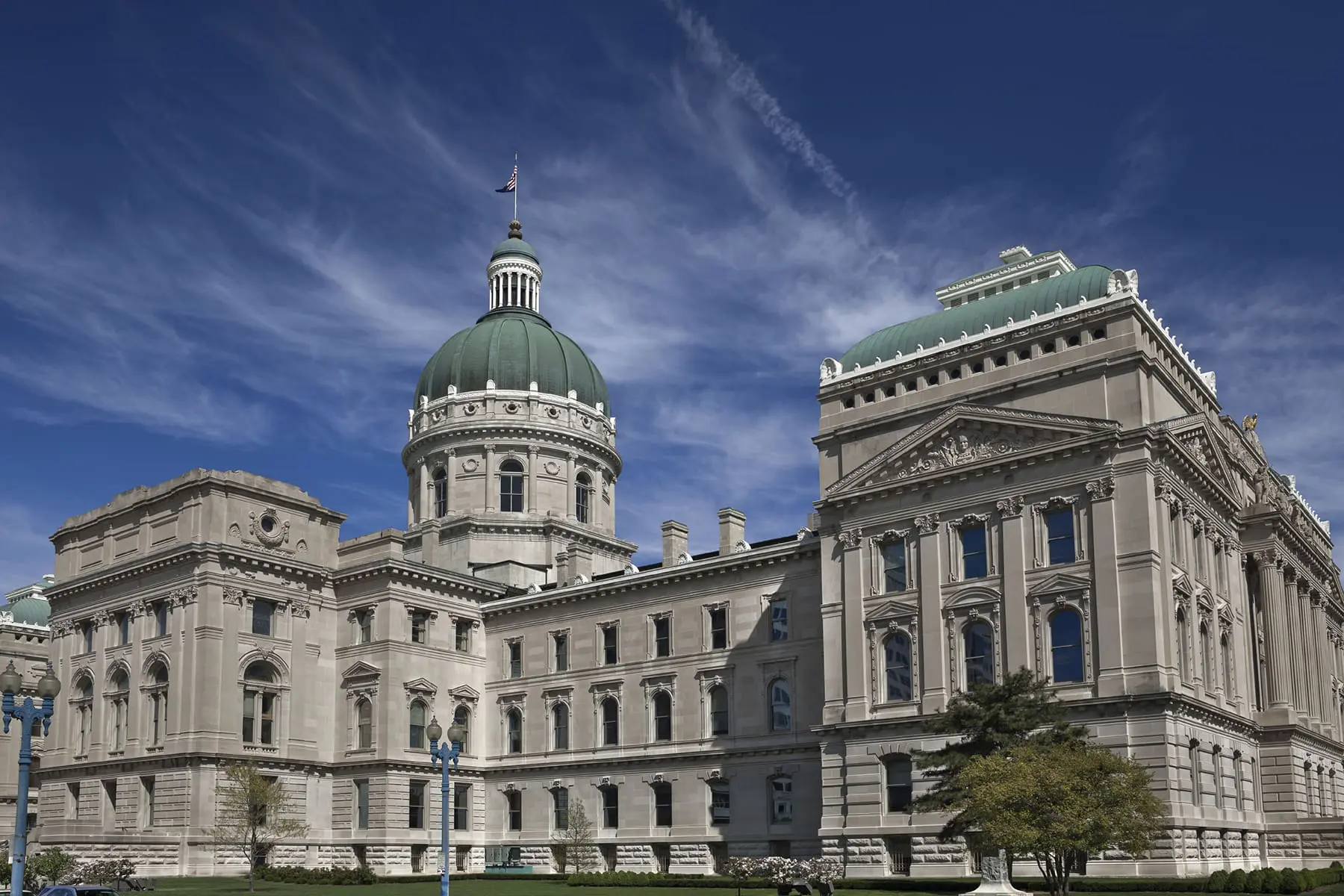 A stately capitol building with a dome and classical architecture stands under a blue sky with scattered clouds.