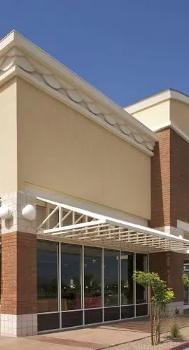 A modern retail building with a covered walkway, large windows, and an arched entrance under a clear blue sky.