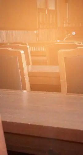 Empty wooden chairs and desks are basking in the warm glow of sunlight, suggesting a peaceful setting, perhaps in a lecture hall or courtroom.