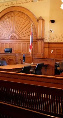 A traditional courtroom with a judge's bench, witness stand, seating for the public, and American and state flags.