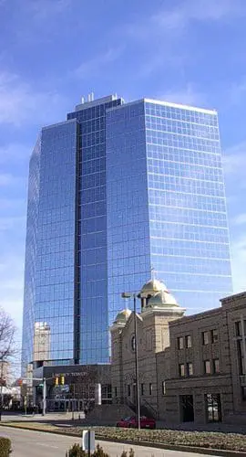 A tall glass skyscraper overlooks smaller traditional buildings under a clear blue sky.