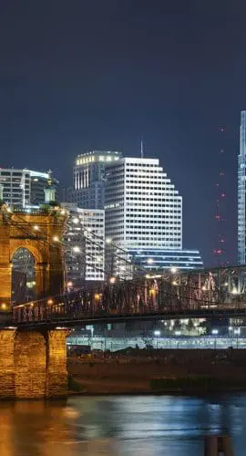 A nighttime cityscape showcases illuminated buildings and a bridge over a river, highlighting an urban skyline.