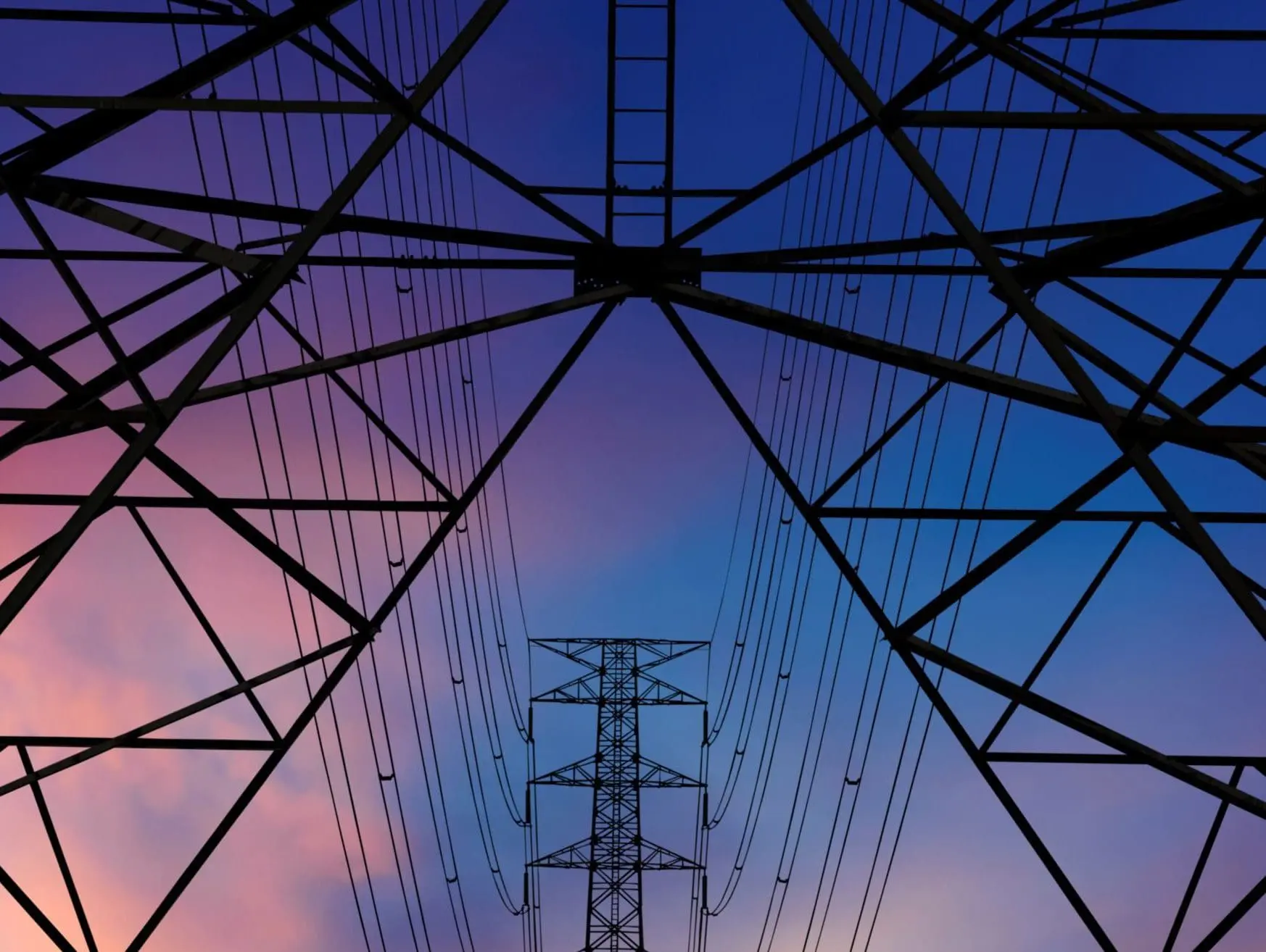 A view looking upward at an electricity pylon against a twilight sky.