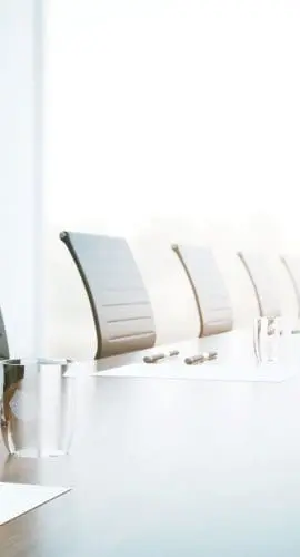 A row of black chairs alongside a modern conference table with a glass of water, indicating a professional or business setting, with bright natural light in the background.