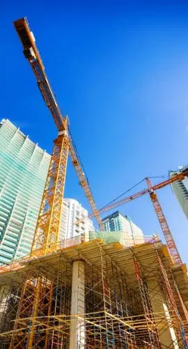 A construction site with scaffolding, cranes, and tall buildings under a blue sky.