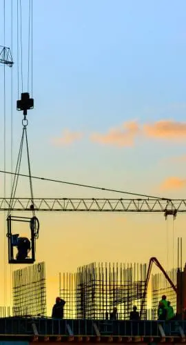 Silhouetted construction cranes tower over a building site against a sunset sky.