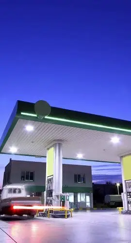 A gas station is illuminated at dusk with a clear blue sky in the background.