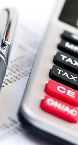 A calculator with a prominent red "TAX" button is lying next to a pen on top of financial documents.