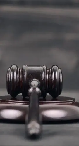 A wooden judge's gavel rests on its sound block on a dark wooden background, symbolizing law and authority.