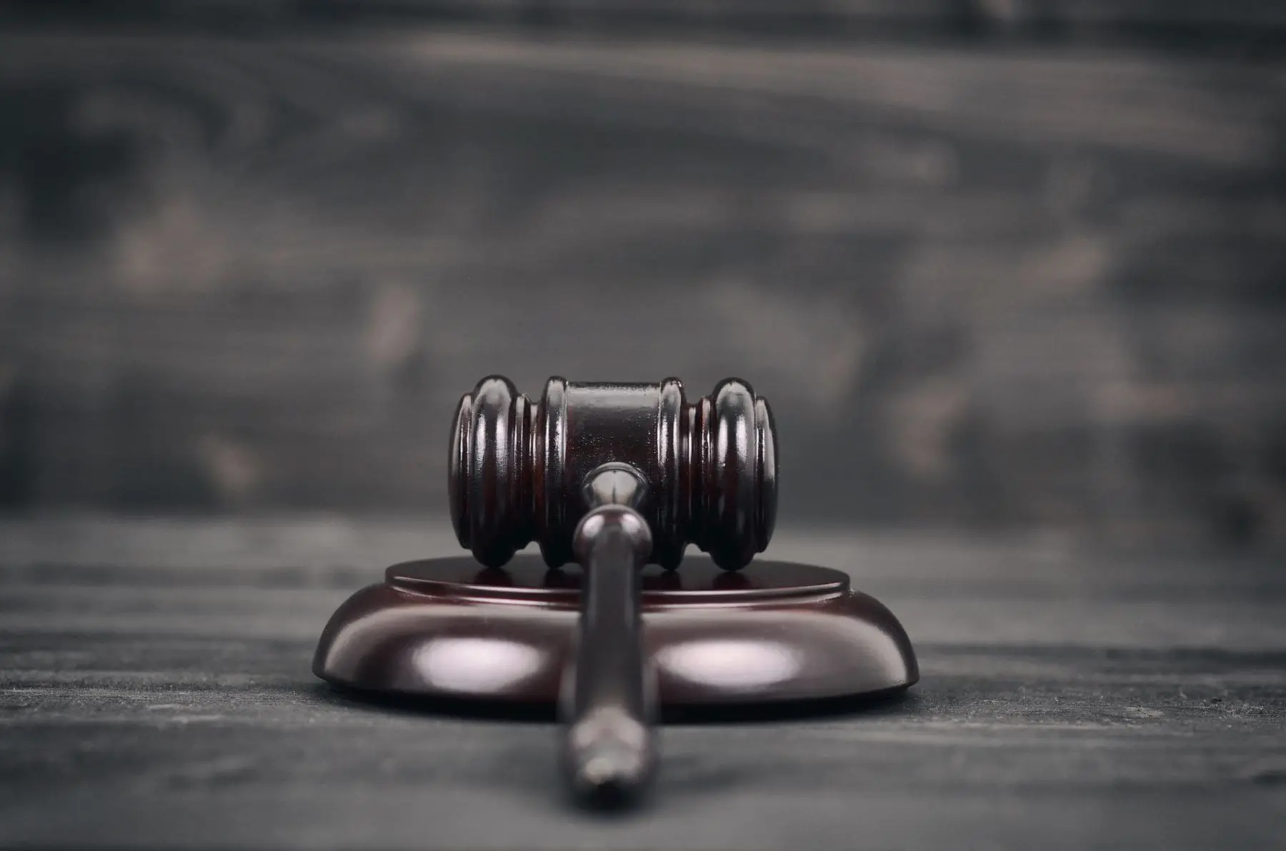 A wooden judge's gavel rests on its sound block on a dark wooden background, symbolizing law and authority.