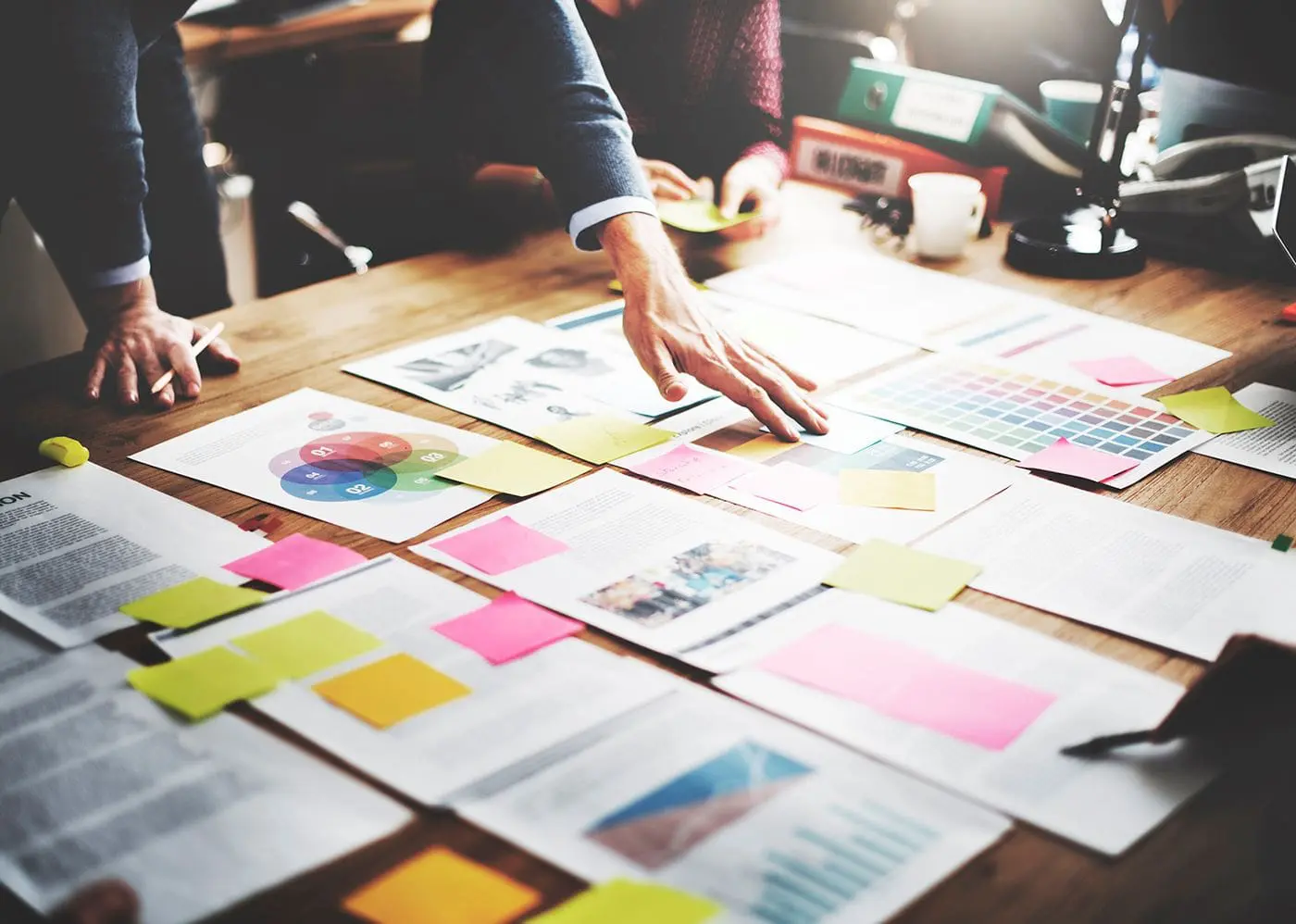 A group of individuals are collaborating over a table scattered with papers, sticky notes, and design materials.