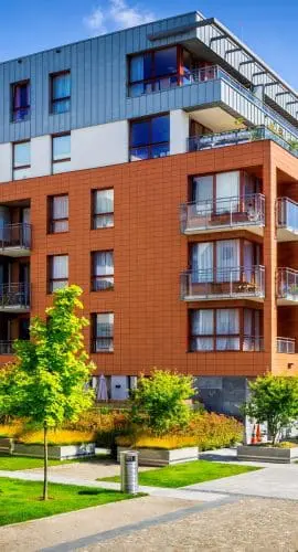 Modern apartment buildings with vibrant facades are surrounded by neatly landscaped green spaces and pedestrian paths under a clear blue sky.