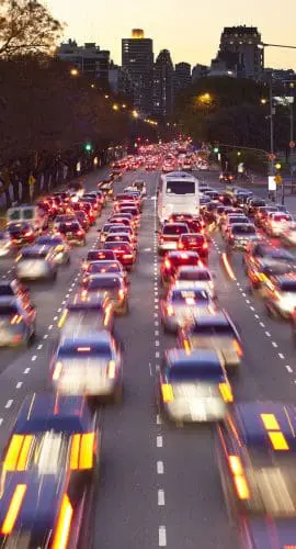 A bustling city street at dusk with blurred vehicles indicating heavy traffic and motion.