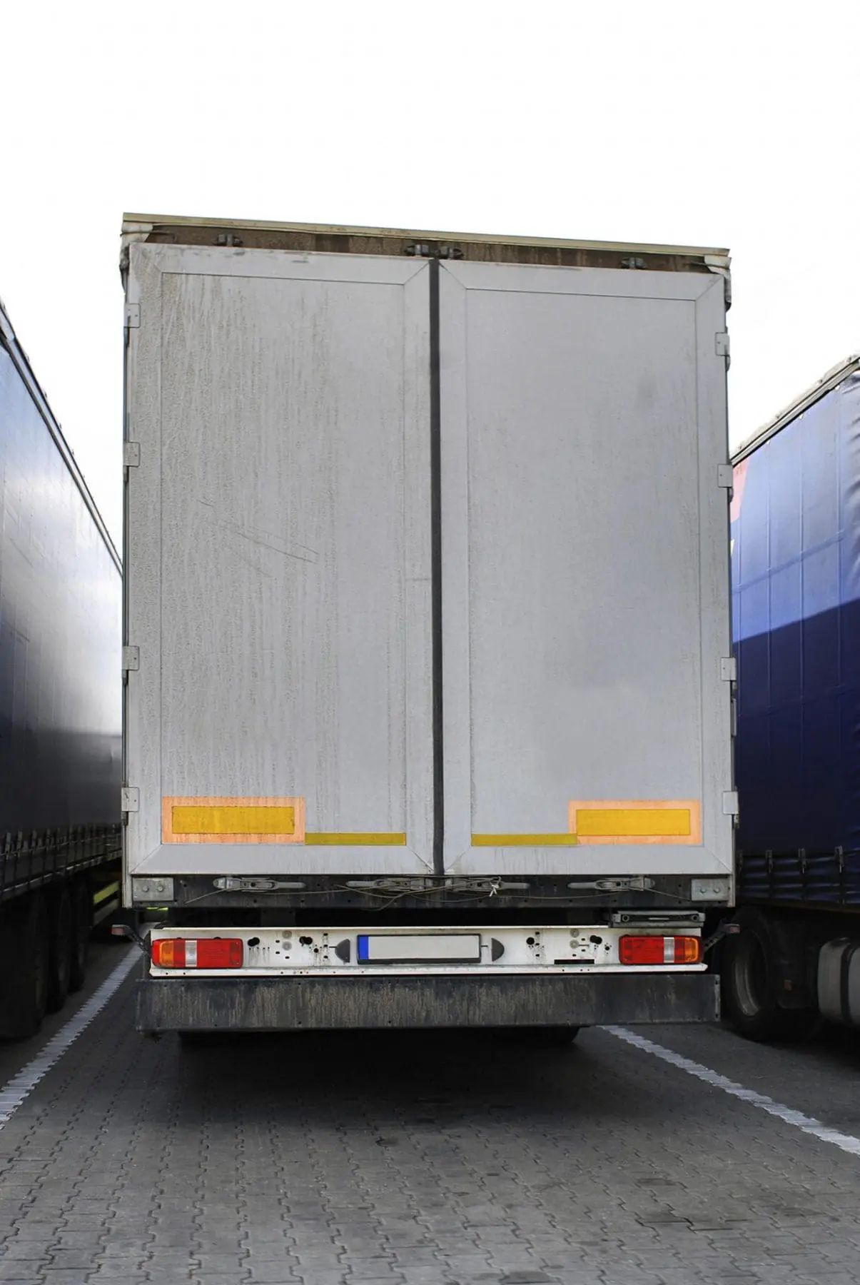 A large, closed, grey cargo truck with reflective stripes is parked between two similar vehicles.