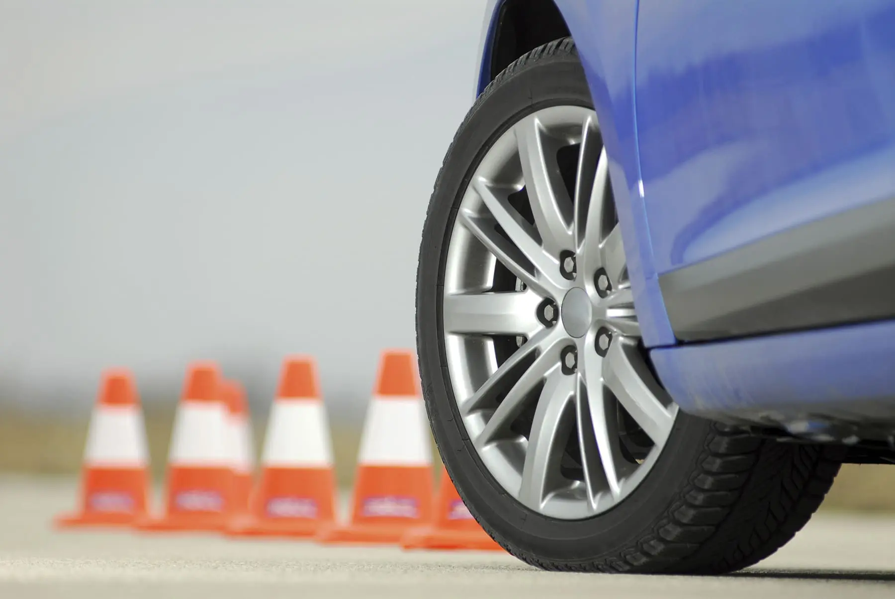 A blue car is parked near a row of orange traffic cones, likely indicating a driving test or parking practice area.