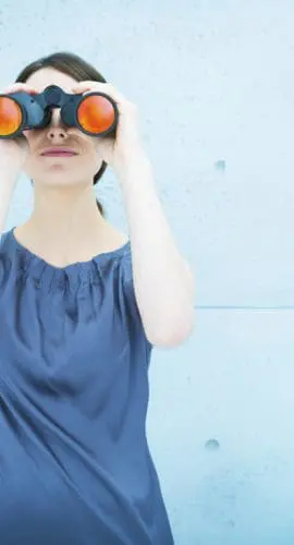 A person is looking through a pair of orange binoculars against a blue background with a subtle pattern.