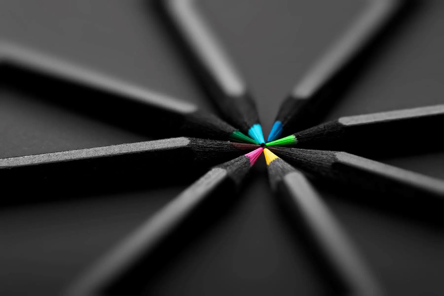 A close-up view of several pencils arranged in a circle with tips meeting in the center, highlighting the contrast between the colorful tips and the dark background.