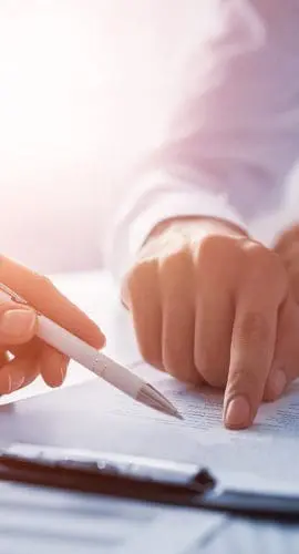 A person is reviewing a document with a pen in hand, ready to write or make annotations.