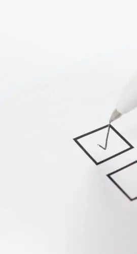 A hand holding a pen appears to be ticking a checkbox on a paper form.