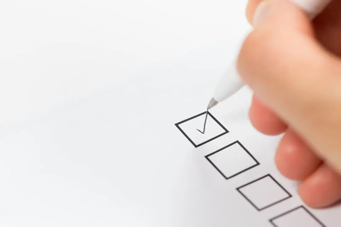 A hand holding a pen appears to be ticking a checkbox on a paper form.