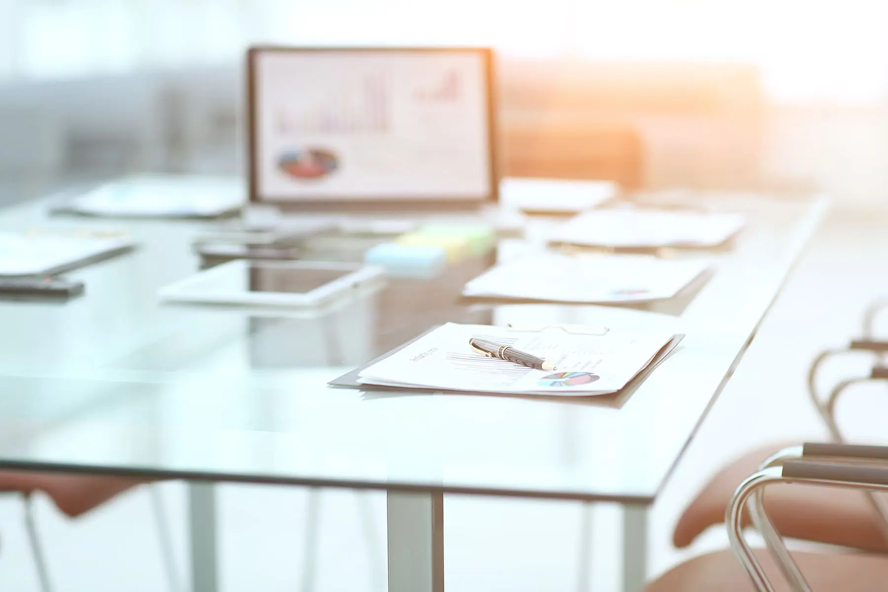 A modern office setup with a desk, documents, and a laptop, illuminated by warm sunlight.