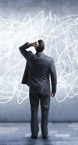 A person in a suit stands confused in front of a chaotic, scribbled mess on a wall.