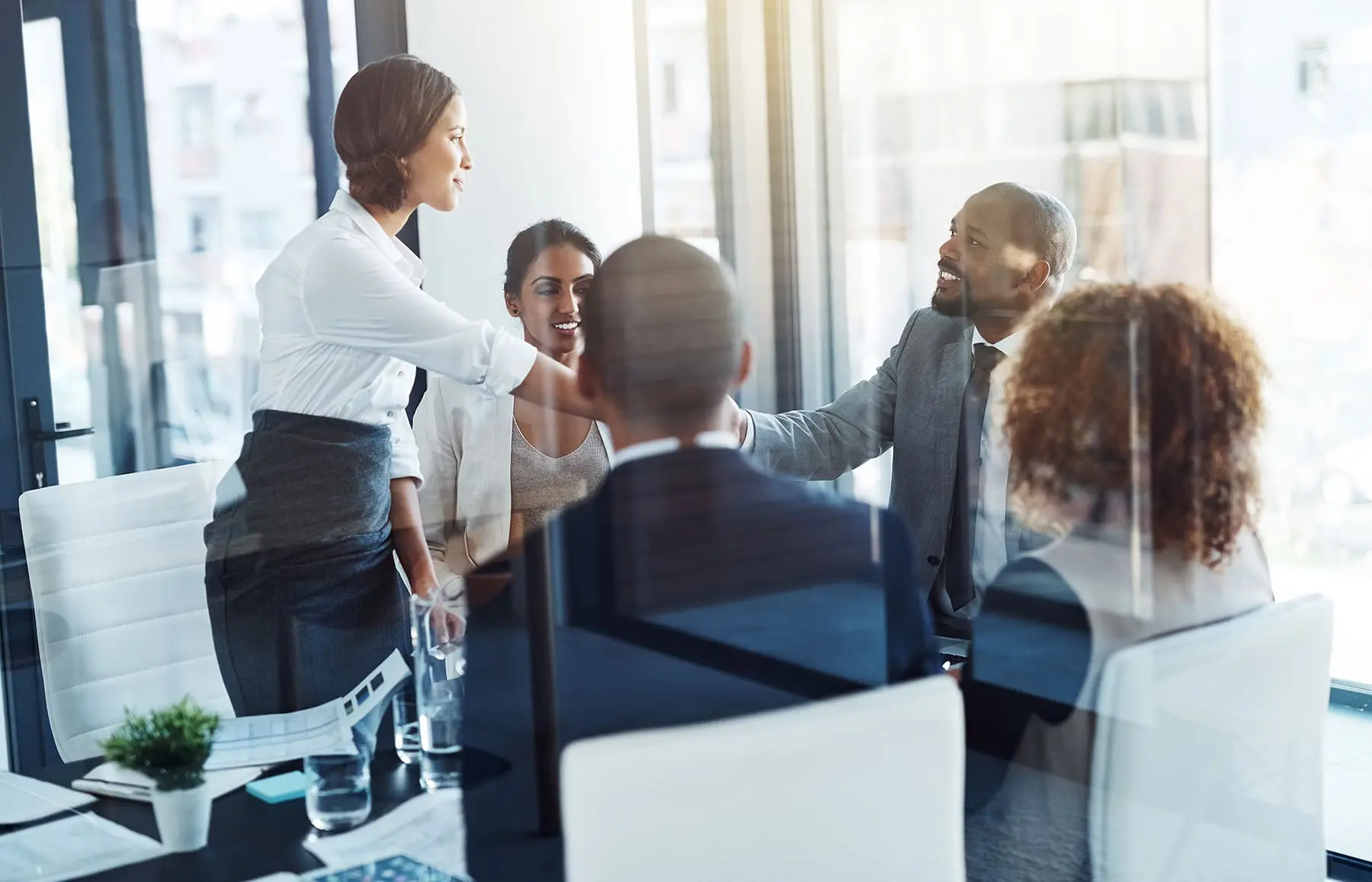 Professionally dressed individuals are engaged in a discussion around a table in a bright office setting.