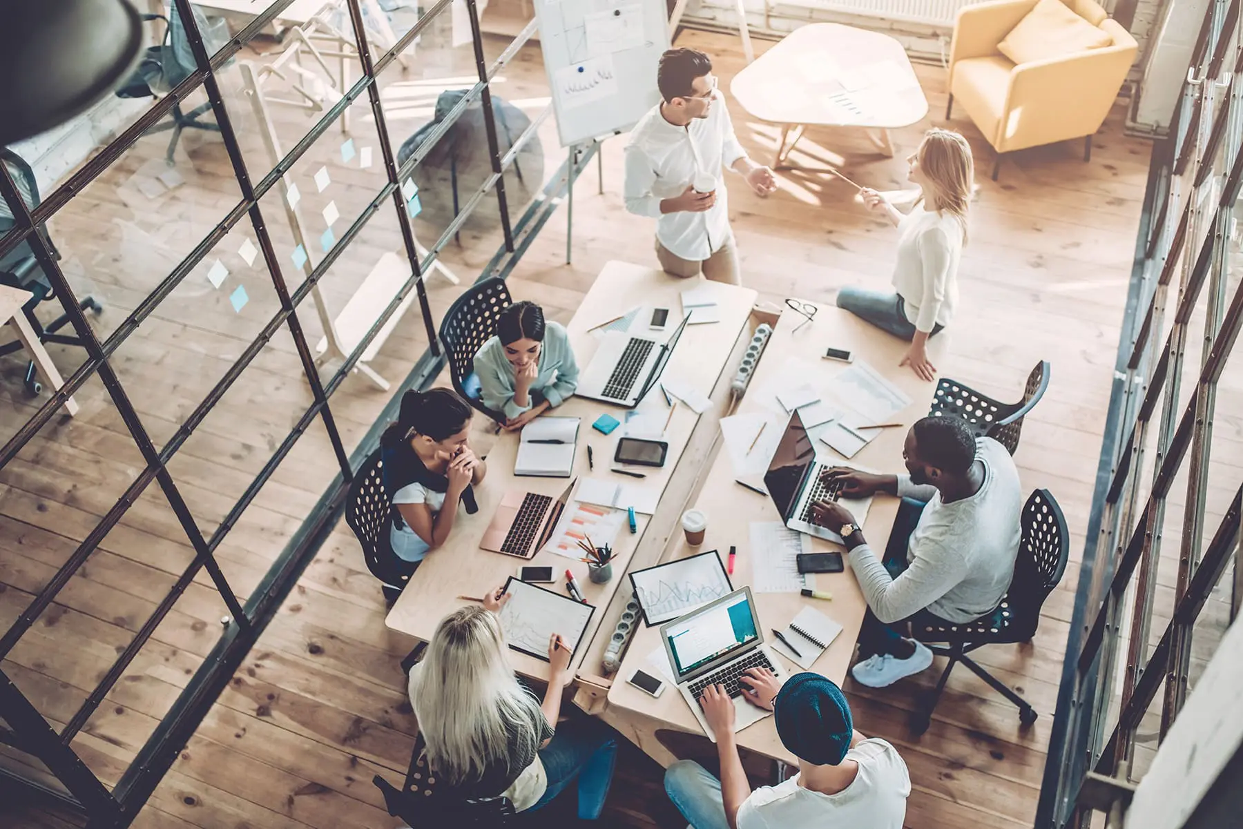 A group of individuals collaborates around a table filled with laptops and documents in a modern office setting.