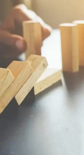 A hand is initiating a chain reaction by knocking over a row of standing wooden dominoes.
