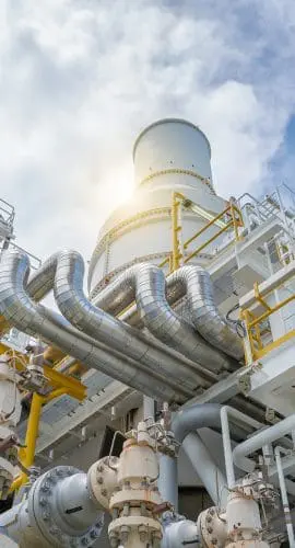 An industrial facility with a complex arrangement of pipes, steel structures, and equipment under a blue sky with clouds.