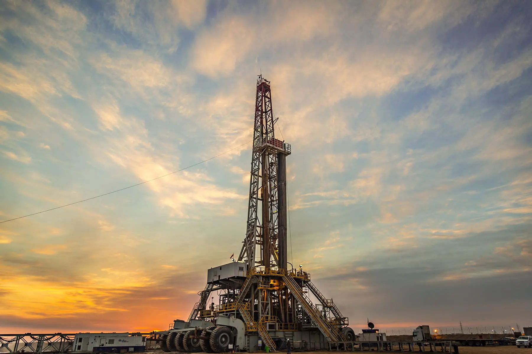 A drilling rig stands against a backdrop of a dramatic sunset sky.