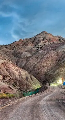 A lit drilling rig stands against a backdrop of rugged hills under a twilight sky.