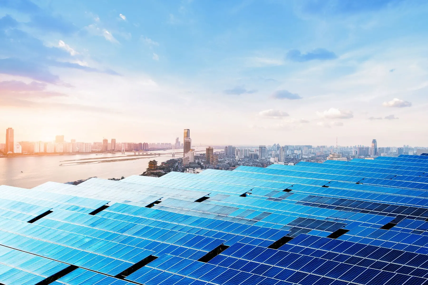 A solar panel array spans the foreground with a sunlit city skyline and clouds in the background.