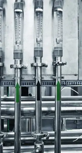 Industrial equipment with several cylindrical glass measuring devices connected to a network of metallic pipes.