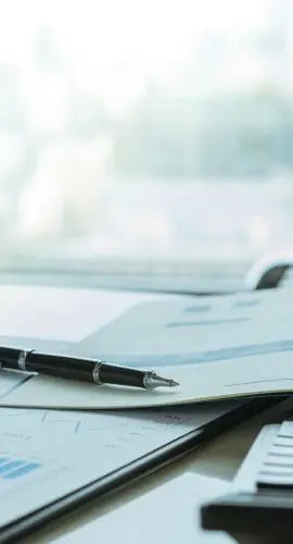 An open notebook with graphs is lying next to a calculator and a pen on a desk, indicative of an office or study environment.