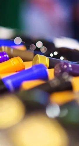 A close-up of a collection of colorful wine bottles lying horizontally with focus on their necks and cap seals.