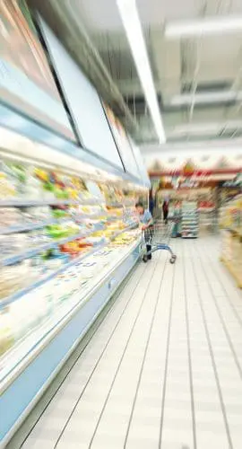 A blurred view of a supermarket aisle with products on shelves and bright lighting, conveying a sense of motion or haste.