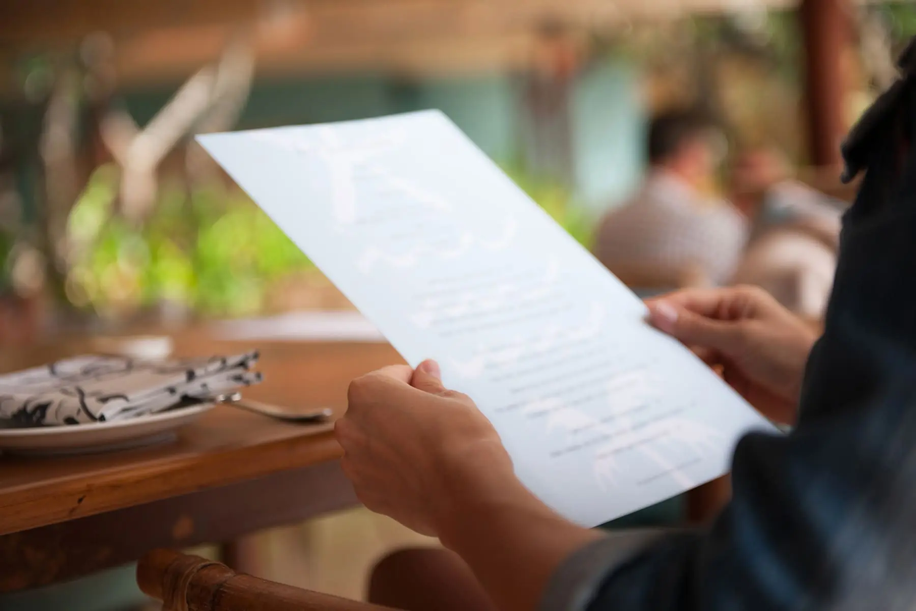 A person is holding a menu at a restaurant table.