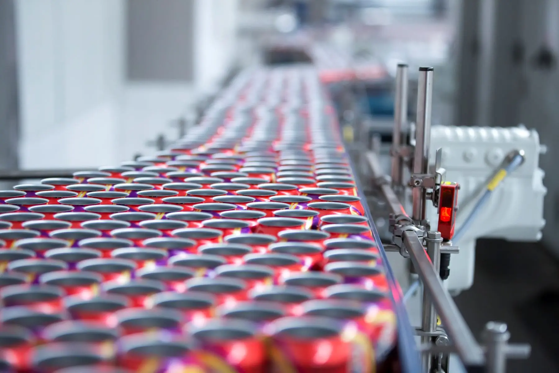 A conveyor belt with rows of red aluminum cans in a manufacturing facility.