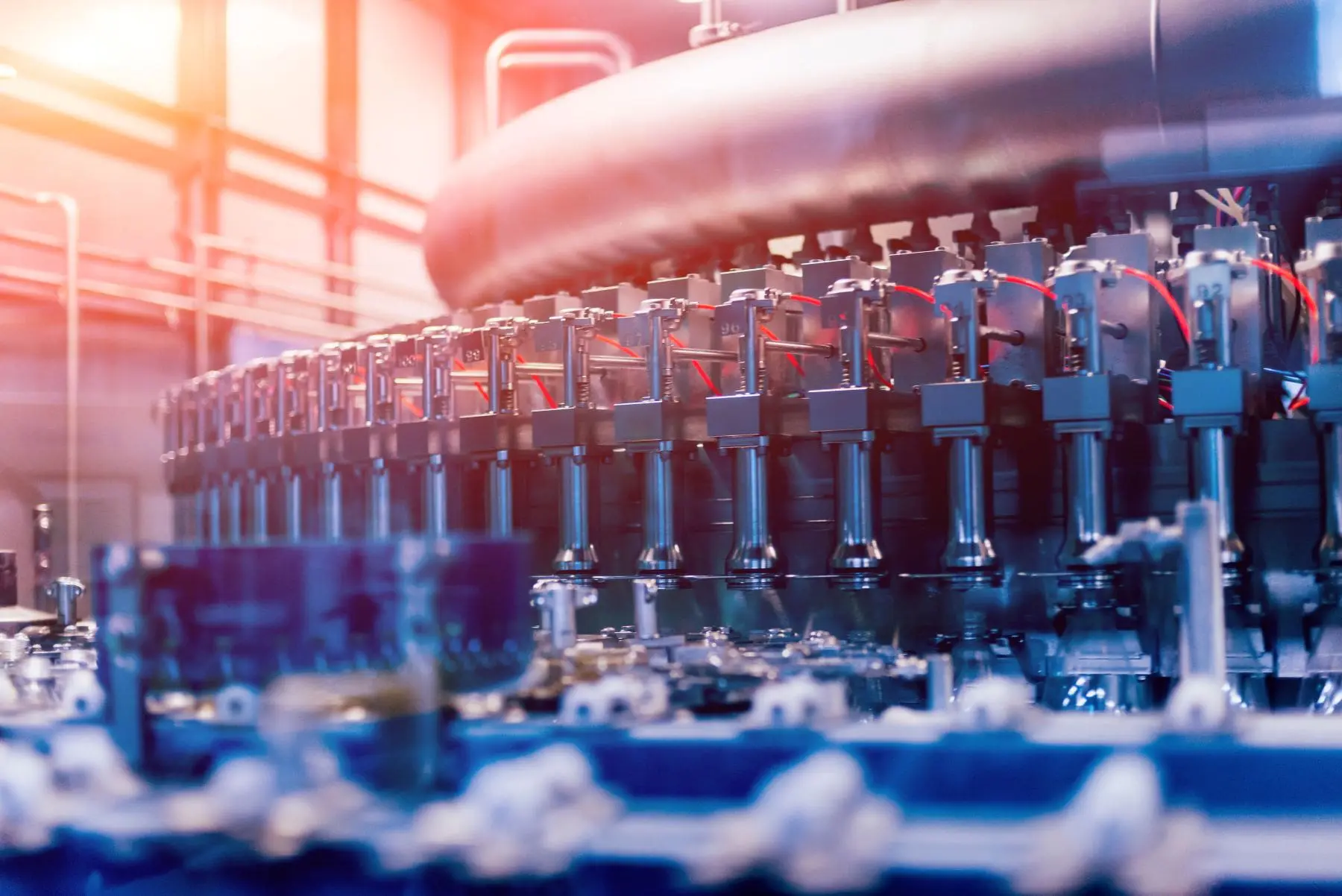 An industrial setting with a focus on a series of metallic cylindrical machinery components, illuminated with blue and warm ambient lights, suggesting a high-tech processing or manufacturing environment.