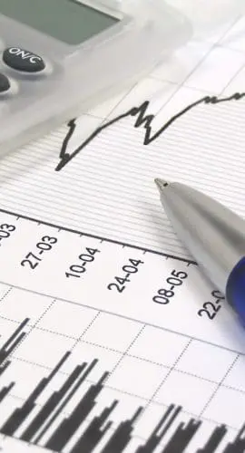 A calculator and pen rest on a sheet of paper with printed financial graphs and data.