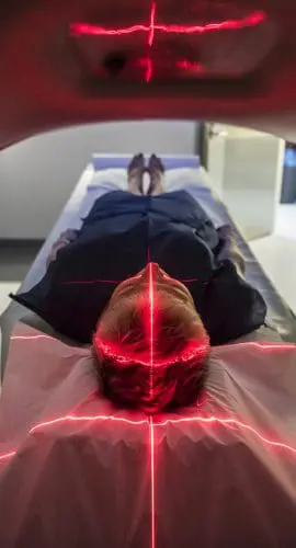 A person lies in a medical scanning device, possibly an MRI or CT machine, with red alignment lasers visible.