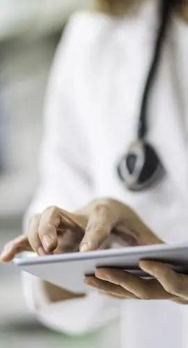 A healthcare professional wearing a white coat and stethoscope is using a digital tablet.