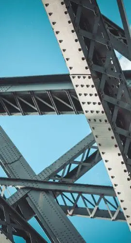 A close-up view of a steel bridge structure against a blue sky with clouds.