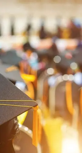 Graduation caps atop heads in a ceremony with sunlit chairs indicating a commencement event.