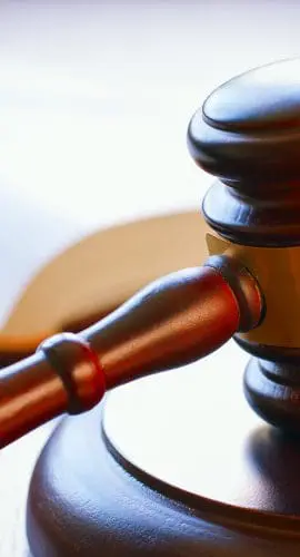 A wooden judge's gavel rests on a sounding block with a blurred legal book in the background.