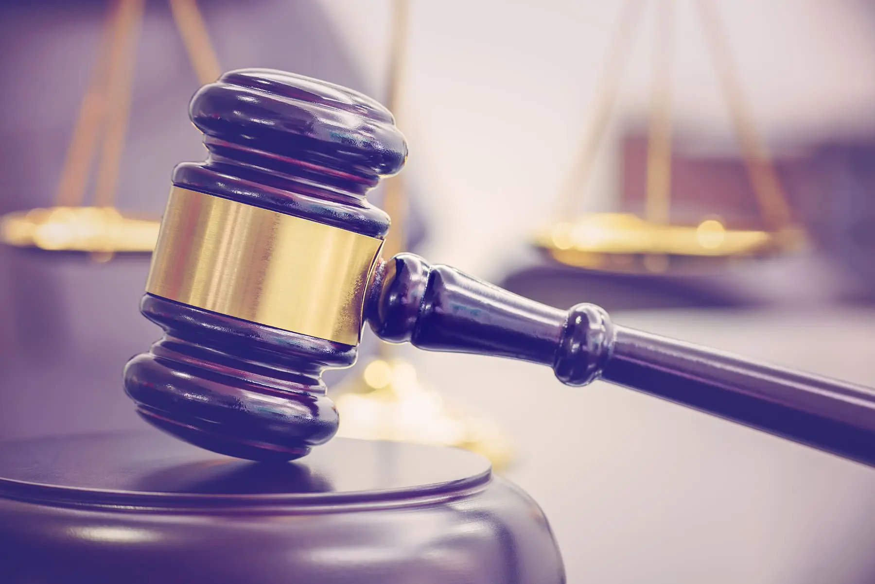 A judge's gavel lies on a surface with a blurred background featuring the scales of justice.