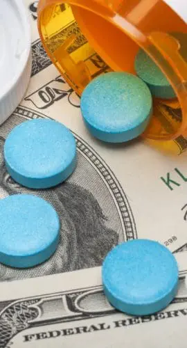 Prescription pills are scattered on a background of US dollar bills next to an open pill bottle and a prescription receipt.