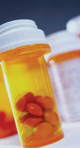 Several prescription medication bottles with orange safety caps, some containing pills, are in focus against a blurred background.
