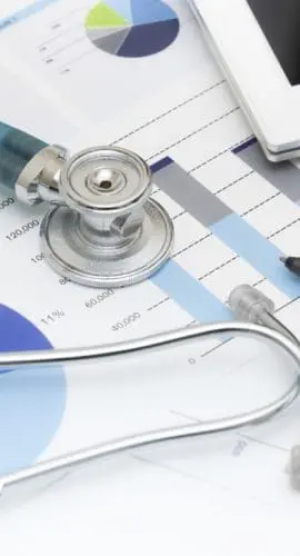 A stethoscope lies atop various charts and reports next to a digital tablet.